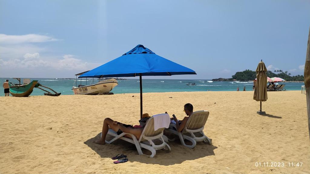 two people sitting in chairs under an umbrella on the beach at Full Moon Resort in Unawatuna