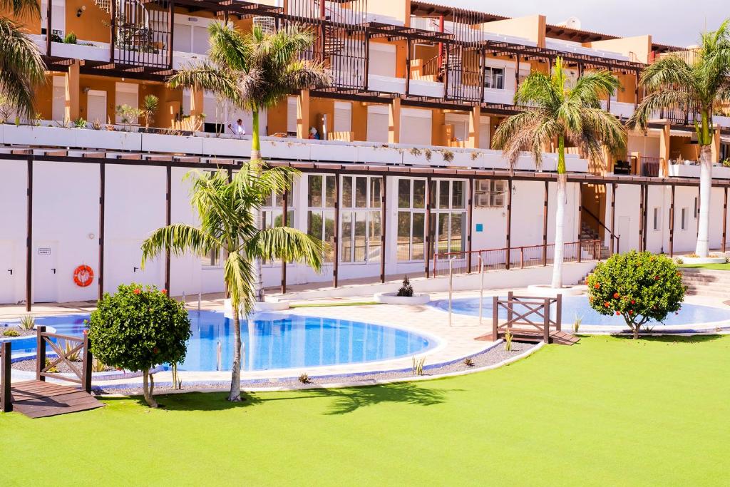 una vista exterior de un edificio con piscina y palmeras en Casa Adosada La Platanera by Vive La Exclusividad, en San Miguel de Abona