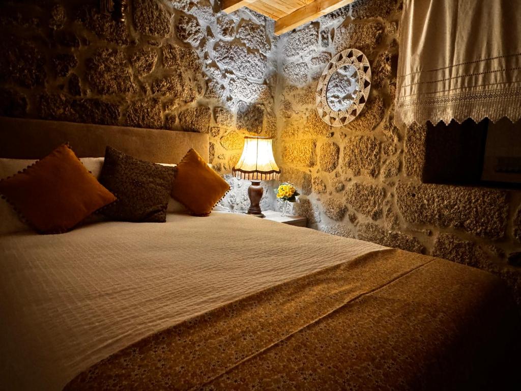 a bedroom with a bed with a lamp and a stone wall at Casa da Vila - Apartamento duplex in Alpedrinha