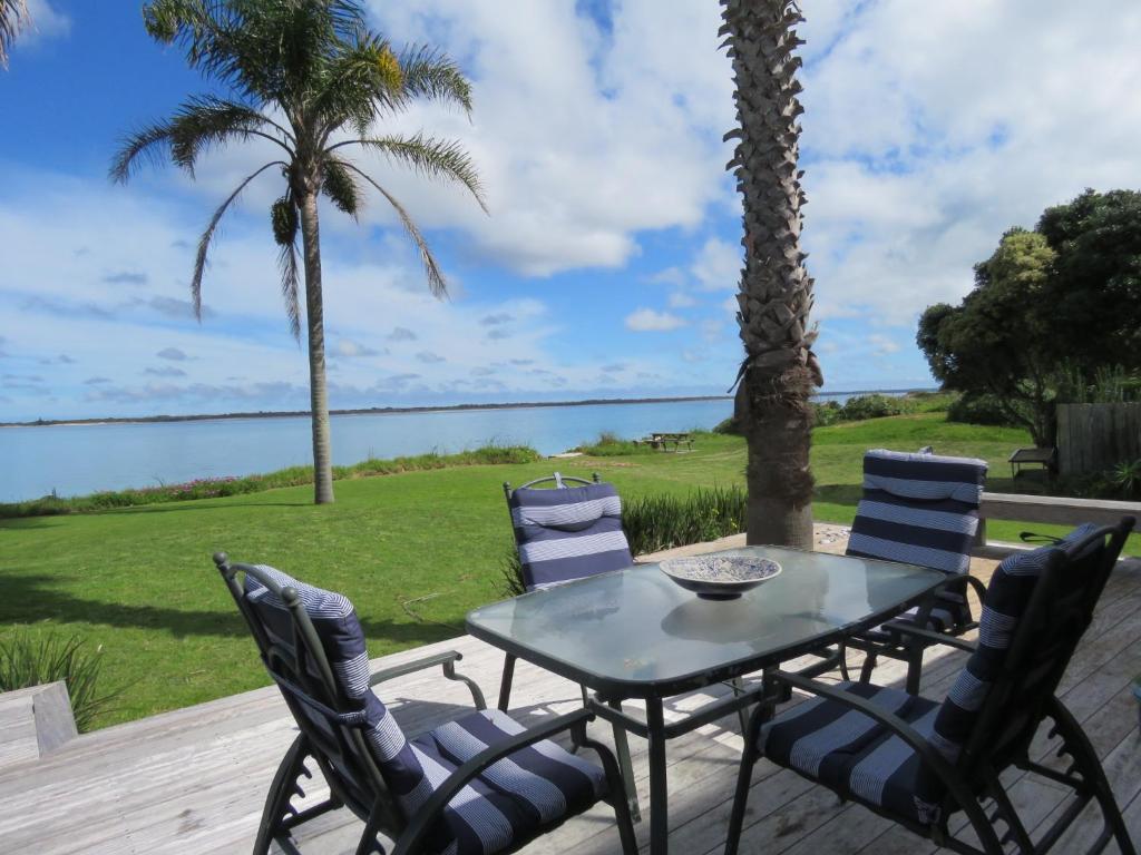 a table and chairs on a patio with a view of the water at Rangiputa Moana in Karikari Peninsula