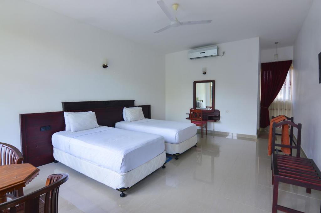 zwei Betten in einem weißen Zimmer mit einem Tisch und einem Schreibtisch in der Unterkunft Siyanco Holiday Resort in Polonnaruwa