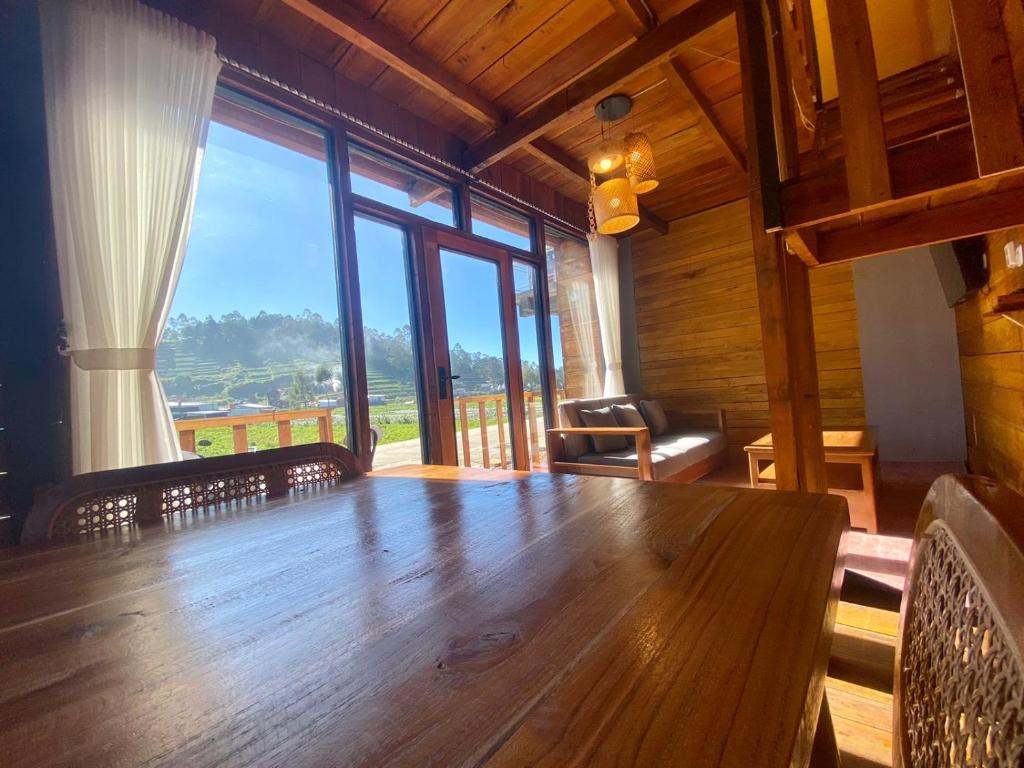 a large wooden table in a room with large windows at Cabin Linggayoni dieng in Dieng