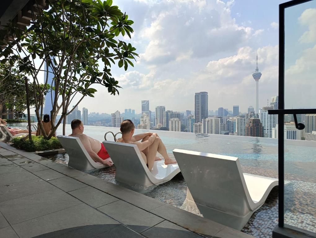 クアラルンプールにあるKLCC Suites At Axon Residenceのスイミングプールの端の椅子に座って2名