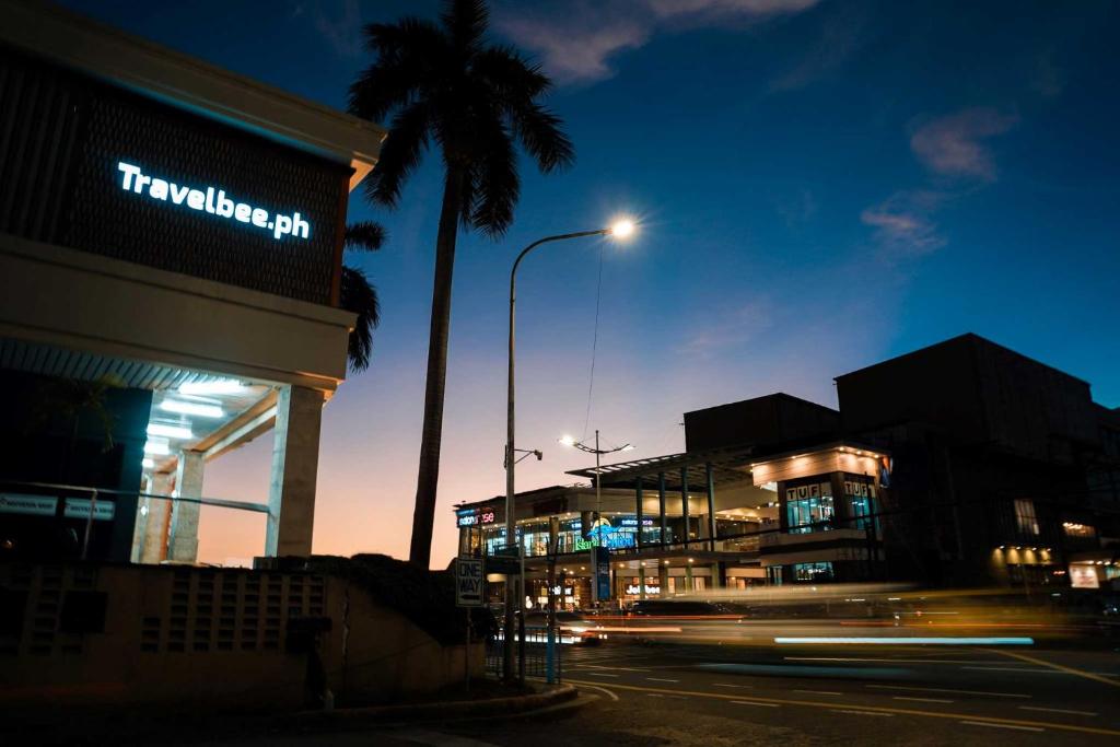 a city street with a building and a palm tree at night at Travelbee Airport Inn in Mactan