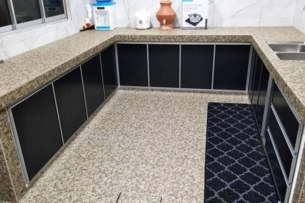 - un comptoir de cuisine avec des placards noirs et un évier dans l'établissement Homestay Dahlia, à Teluk Intan