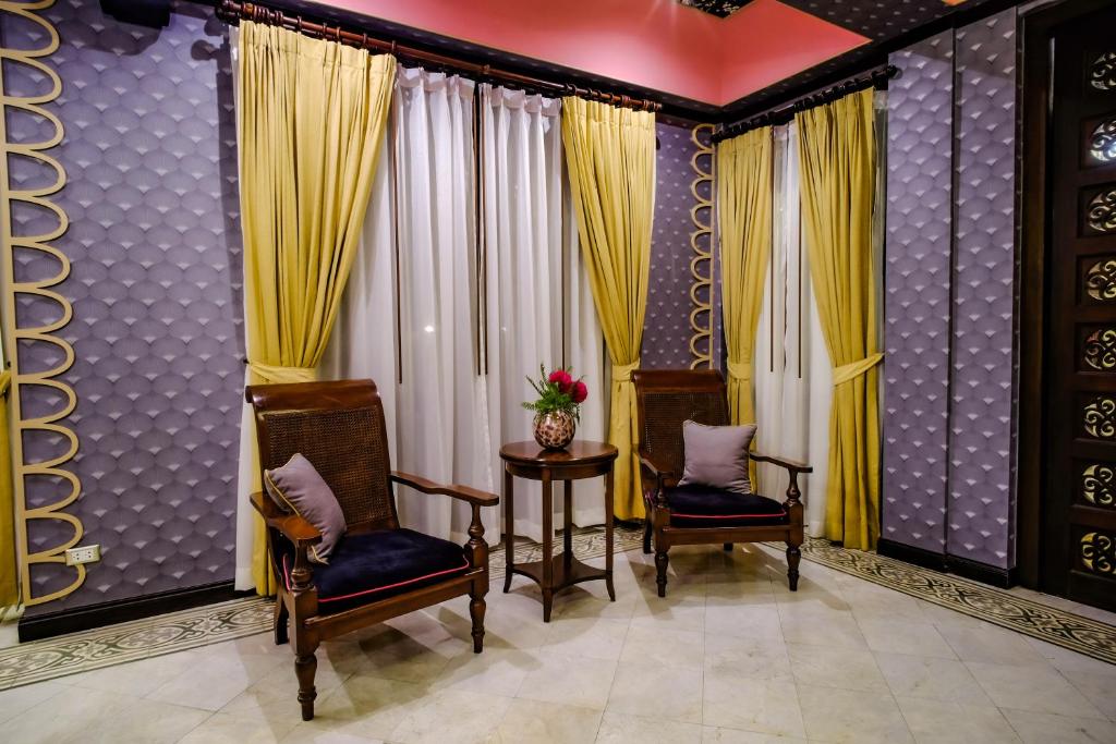 A richly decorated sitting area with two upholstered armchairs beside curtained windows.