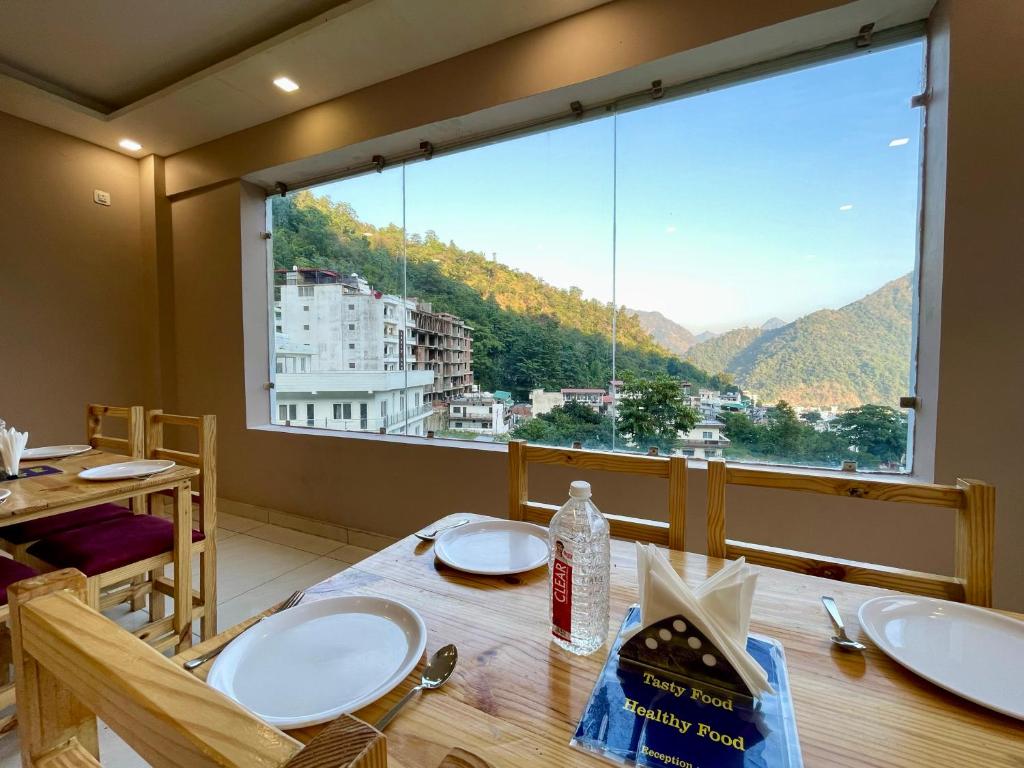 ein Esszimmer mit einem Tisch und einem großen Fenster in der Unterkunft Hotel Shiv Inn Near Secret Waterfall in Rishikesh