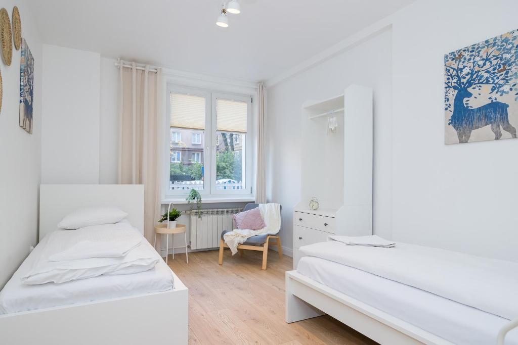 a white bedroom with two beds and a chair at ShortStayPoland Dąbrowszczaków (B138) in Warsaw