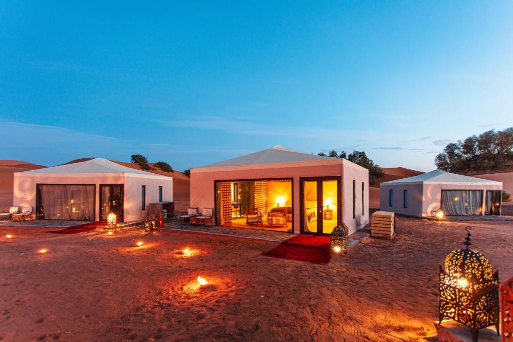 une maison dans le désert la nuit avec des lumières dans l'établissement Merzouga luxury desert camps, à Merzouga