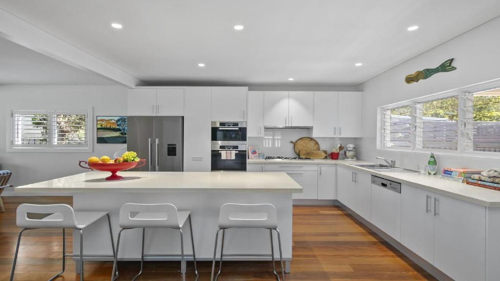 a white kitchen with a large island with bar stools at The Patonga Pearl in Patonga