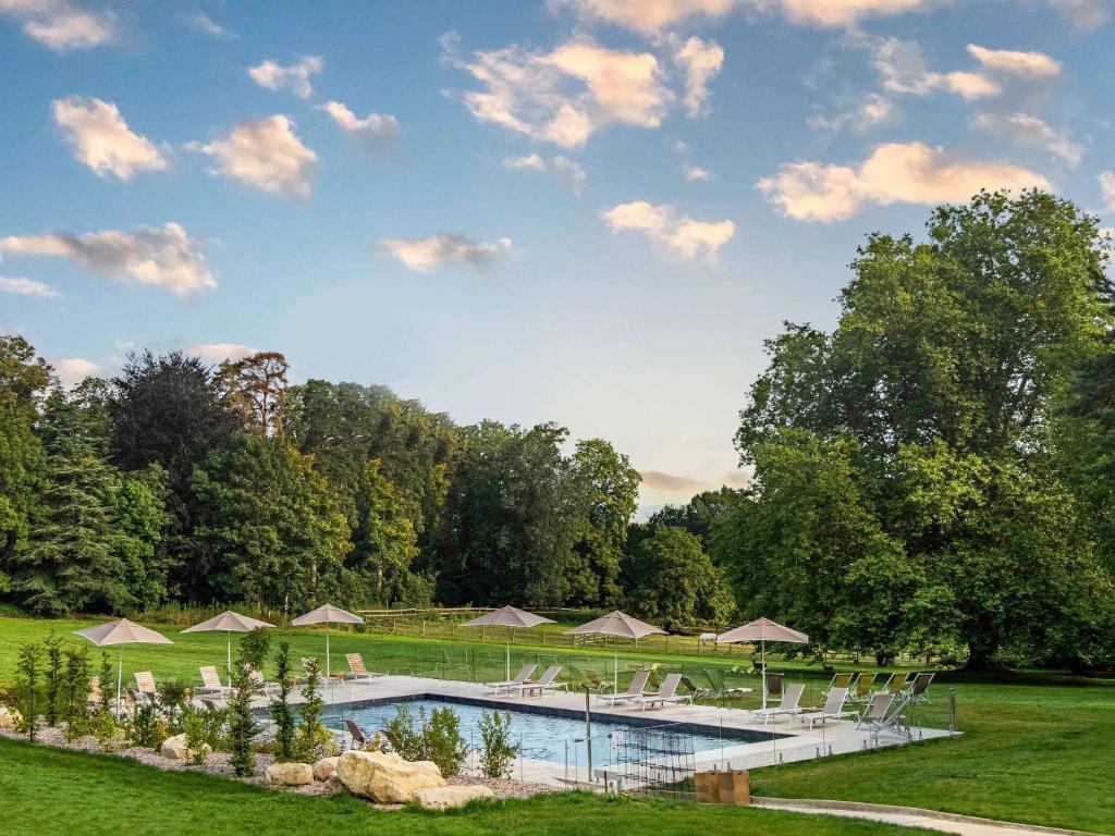 - une piscine avec des parasols et des chaises dans un parc dans l'établissement Novotel Domaine de Maffliers - Paris Val-d'Oise, à Maffliers