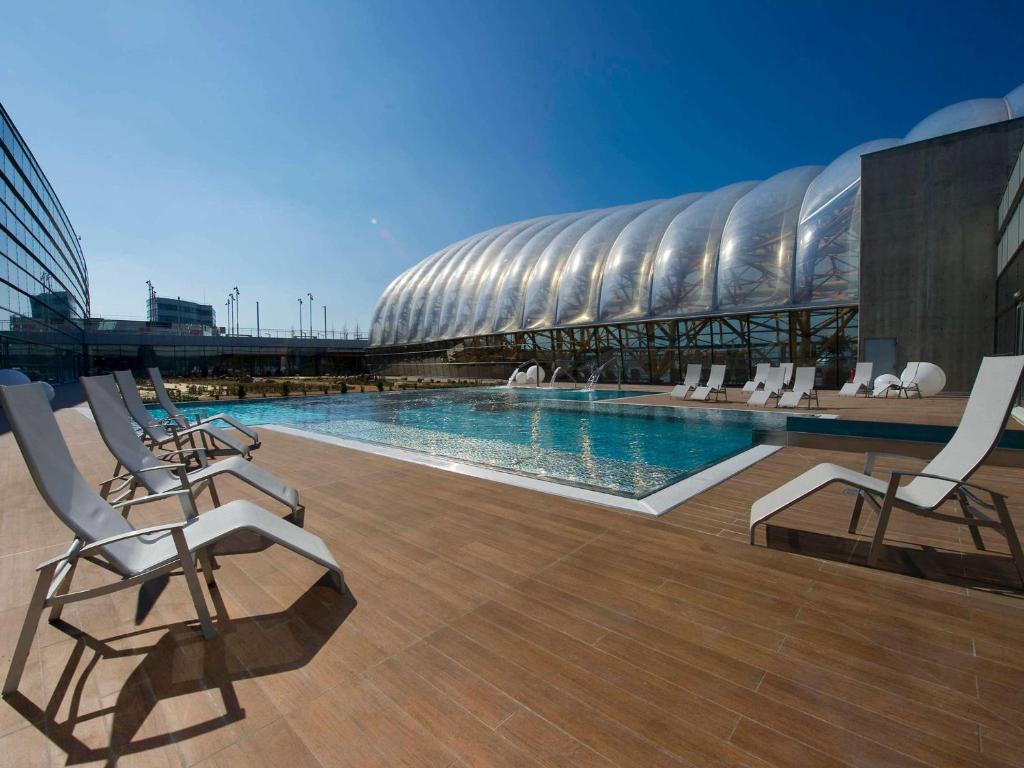 a swimming pool with chairs and a stadium at ibis Styles Saint Julien en Genevois Vitam in Neydens