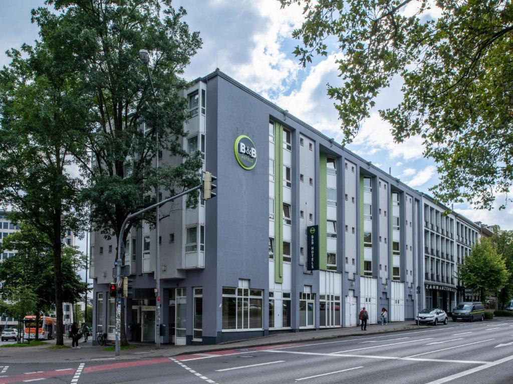 a large white building with green windows on a street at B&B Hotel Aachen-Hbf in Aachen