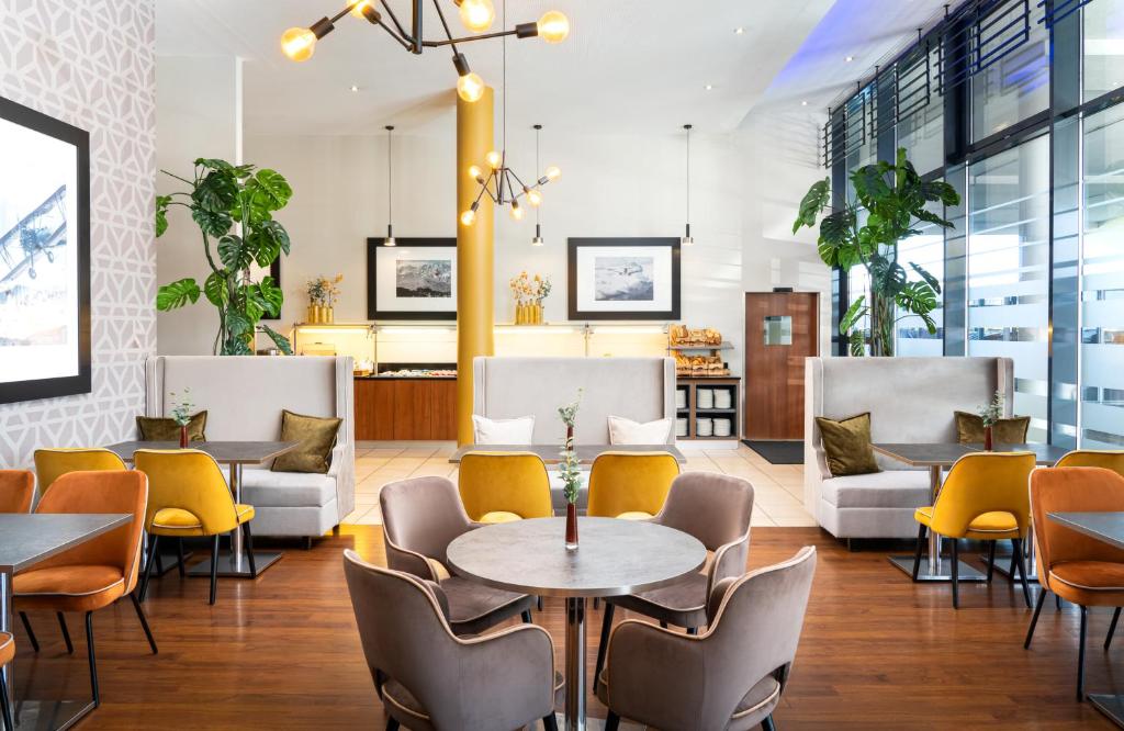 a restaurant with yellow chairs and tables and tablespaces at Leonardo Hotel Salzburg Airport in Salzburg
