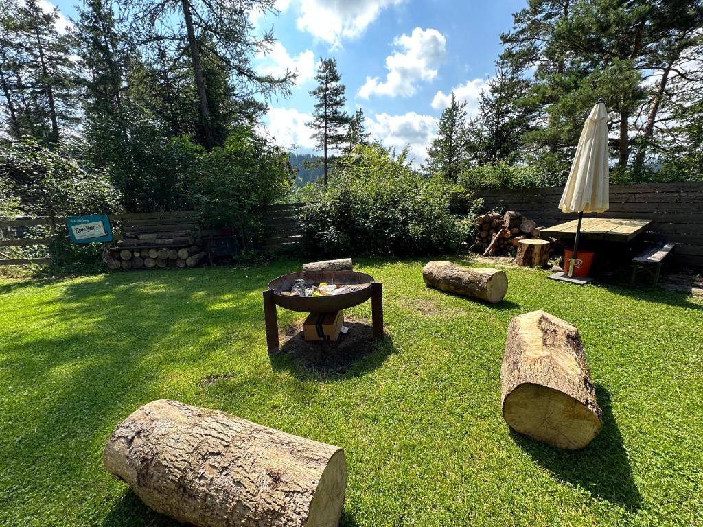 einen Garten mit einem Tisch, Holzscheiten und einem Sonnenschirm in der Unterkunft Ferienhaus im Wald in Edelschrott