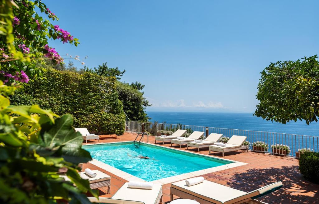 einen Pool mit Stühlen und das Meer im Hintergrund in der Unterkunft Villa Bijoux - Exclusive pool and sea view in Amalfi