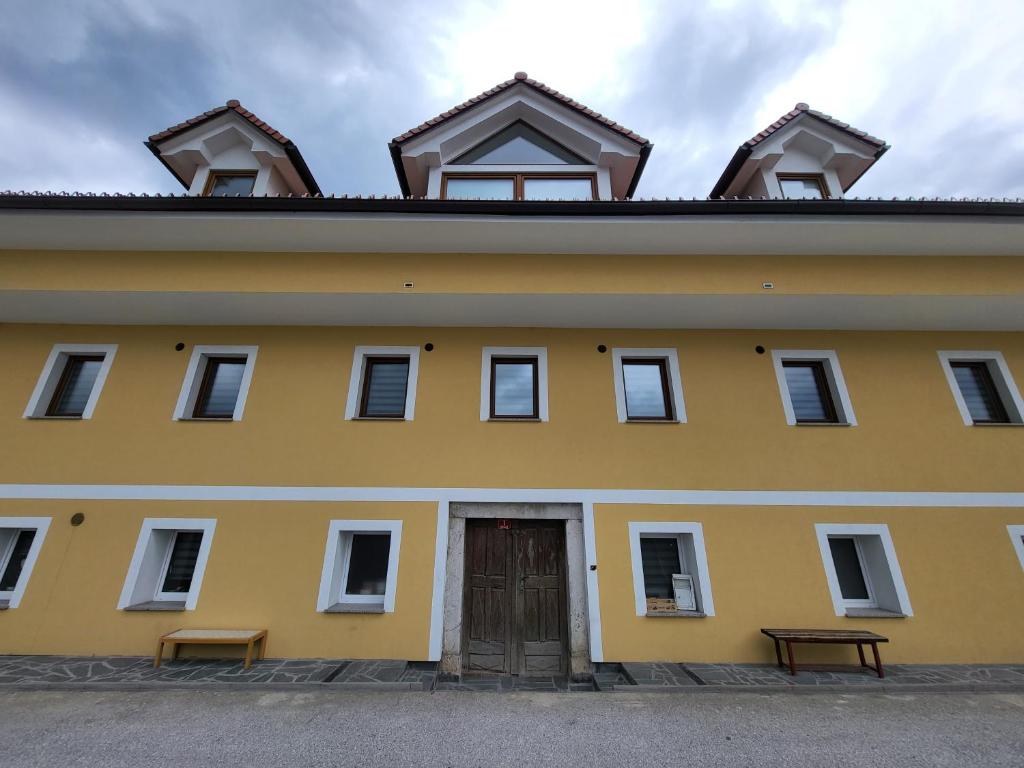 un edificio amarillo con una puerta y dos bancos en Stara Pošta Apartment 1, en Grosuplje