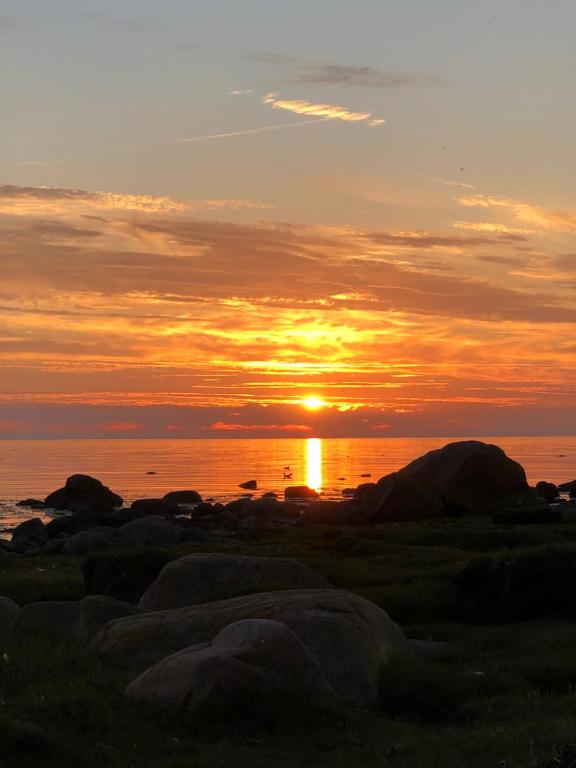 una puesta de sol sobre el agua con rocas y el océano en Havsnära lantligt boende, en Glommen