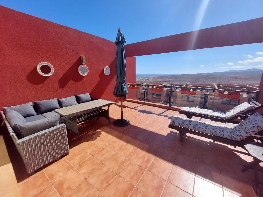 a balcony with a couch and chairs and an umbrella at Casa Bella Vista - pool - WiFi in Caleta De Fuste