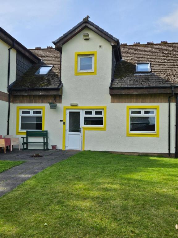 una casa blanca con adornos amarillos y un patio en Cunninghame 3 en Beith