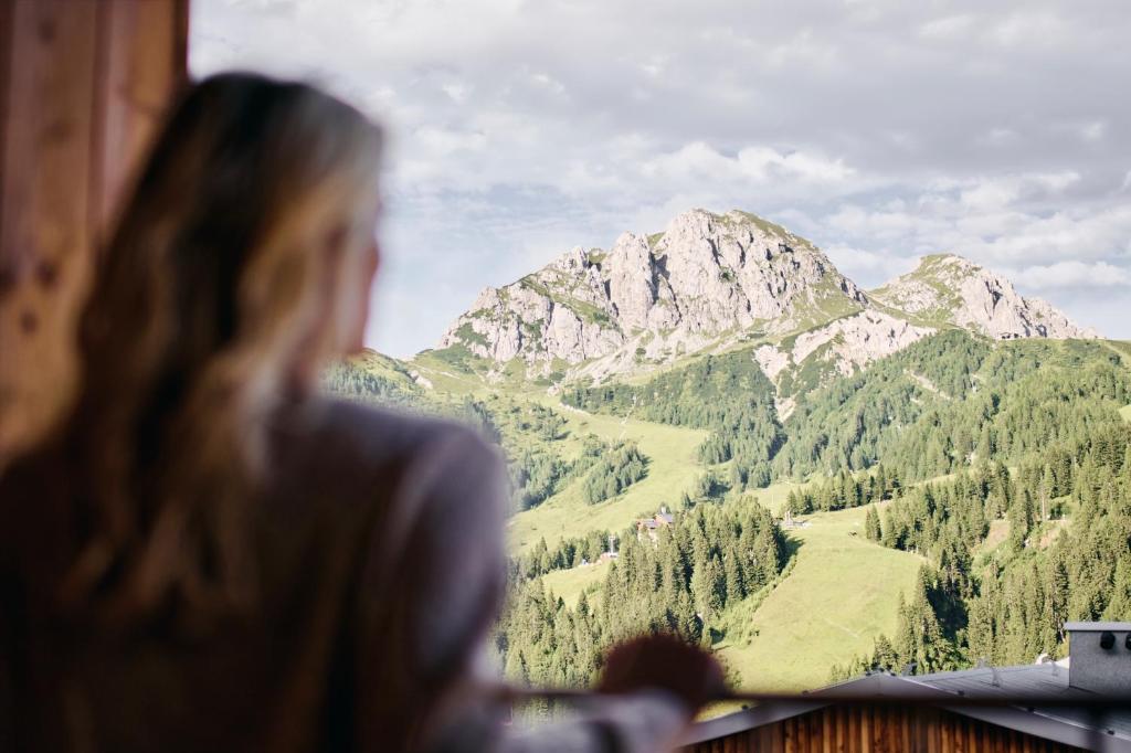 Une femme qui regarde par une fenêtre une montagne dans l'établissement Almresort Sonnenalpe Nassfeld by ALPS RESORTS, à Sonnenalpe Nassfeld
