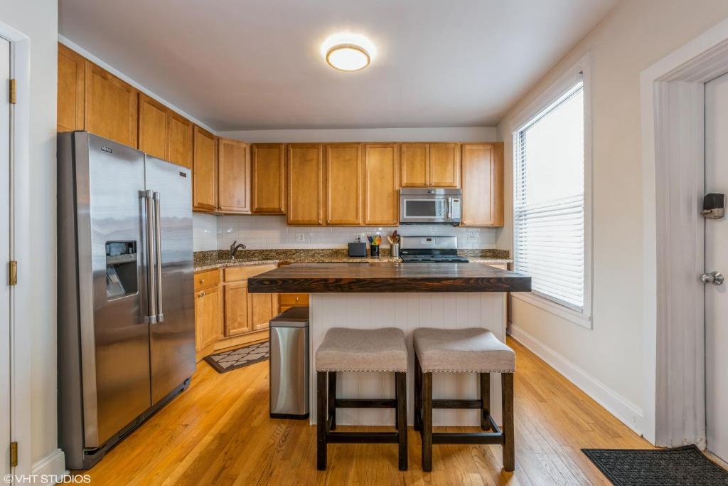 a kitchen with wooden cabinets and a stainless steel refrigerator at Belmont & Racine - Walk to Wrigley & Southport Corridor & Belmont L Train Station! in Chicago