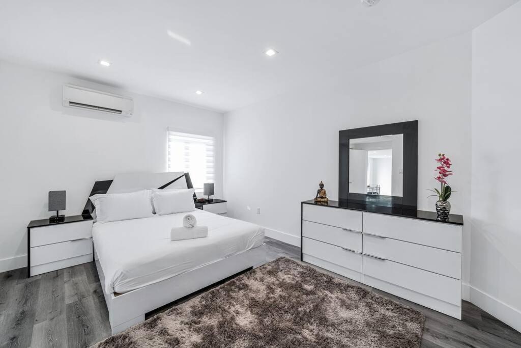 een witte slaapkamer met een bed en een spiegel bij Homey Studio near the Airport and Water Park in Miami