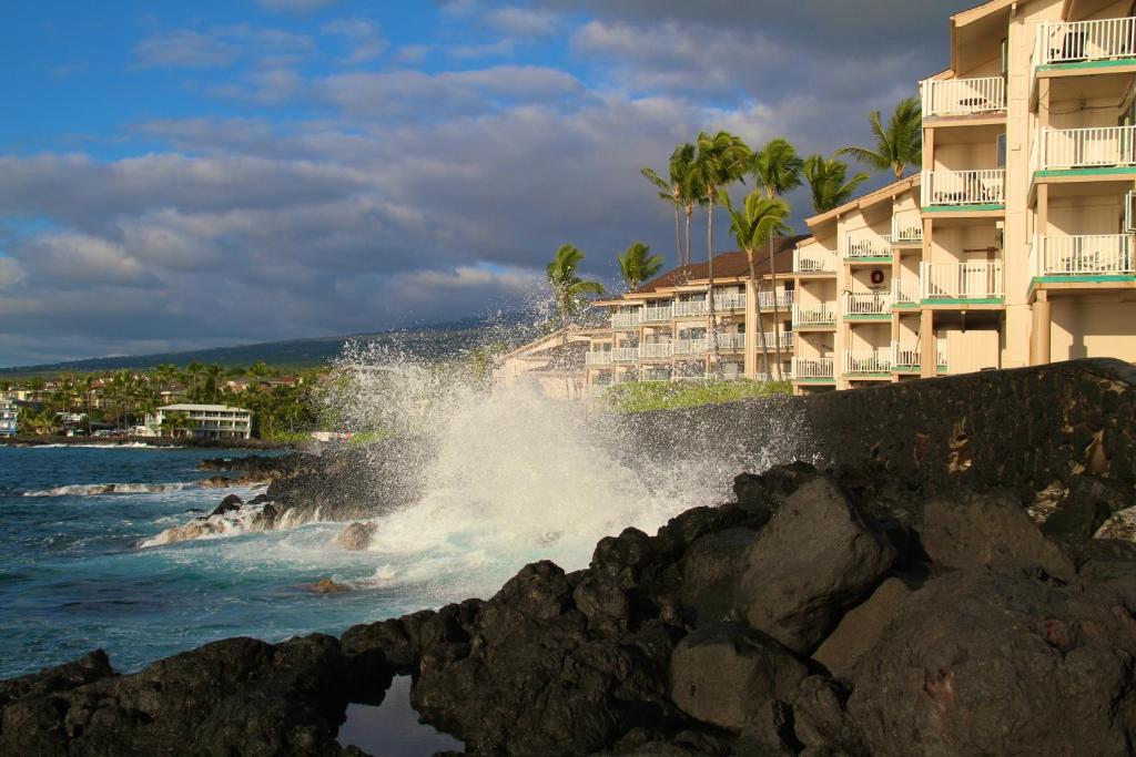 een golf die neerstort op een strand naast gebouwen bij Sea Village in Kailua-Kona