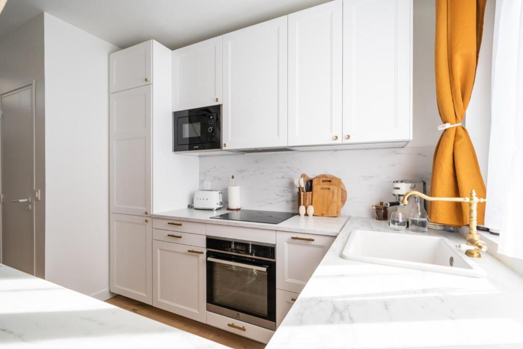 a white kitchen with white cabinets and a sink at Beautiful duplex on the outskirts of Paris - Welkeys in Levallois-Perret