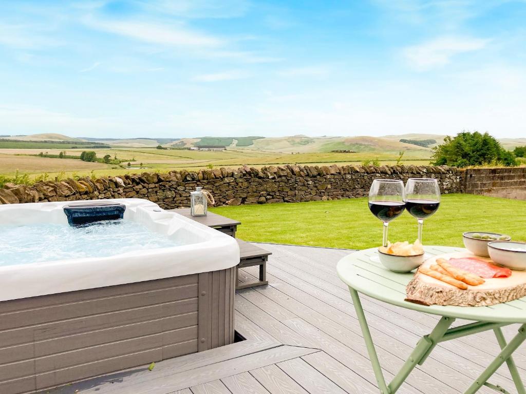 a deck with a hot tub and two glasses of wine at South Riccalton Farm Cottage in Oxnam