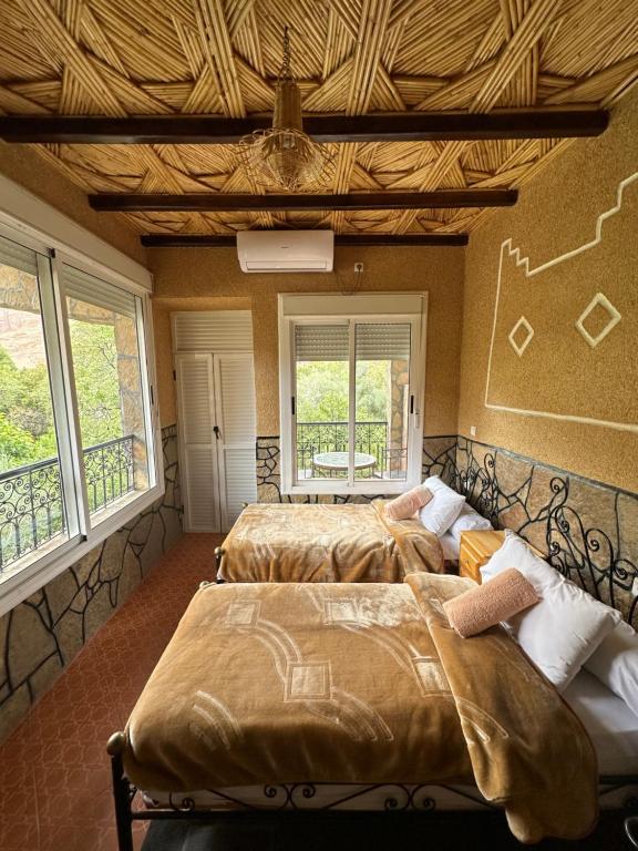 two beds in a room with two windows at La Petite Gorge, H&ocirc;tel & Restaurant Todra Gorge in Tinerhir
