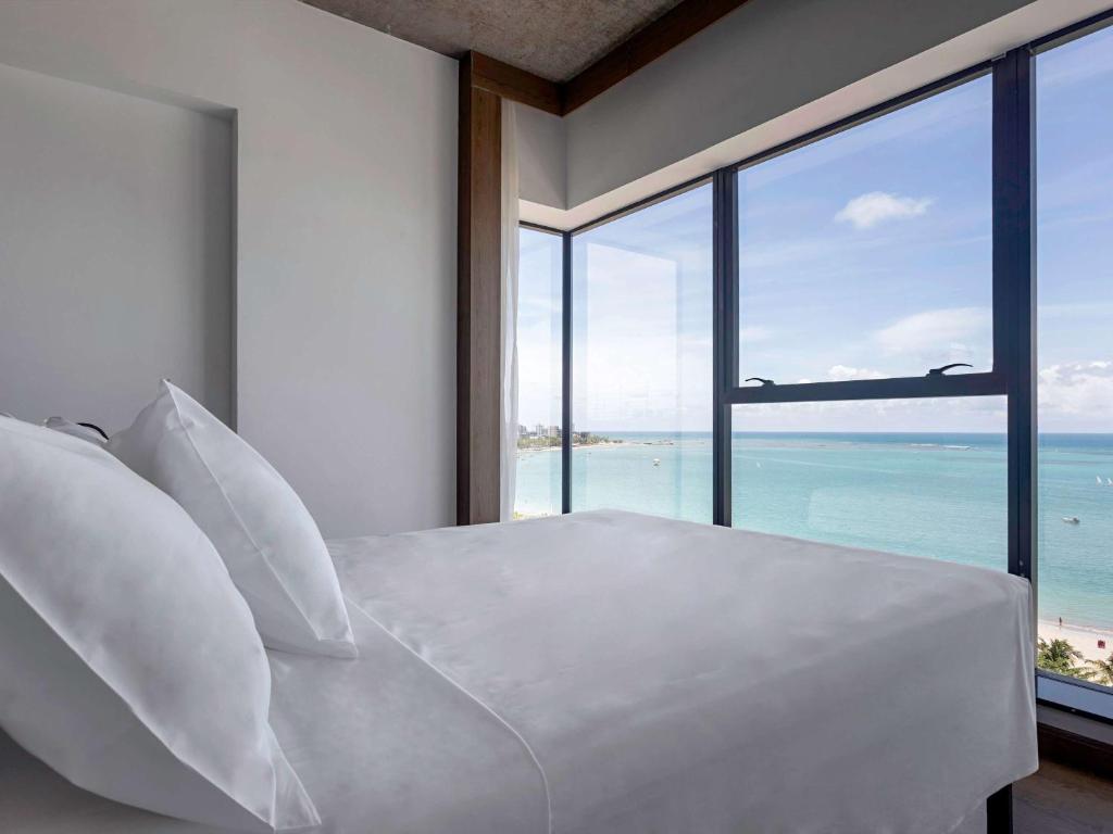 - une chambre avec un lit blanc et une vue sur l'océan dans l'établissement ibis Styles Maceió Pajuçara, à Maceió
