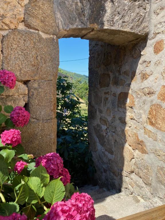 une fenêtre dans un mur de pierre avec des fleurs roses dans l'établissement Le Hameau des Sources, à Colombier-le-Jeune