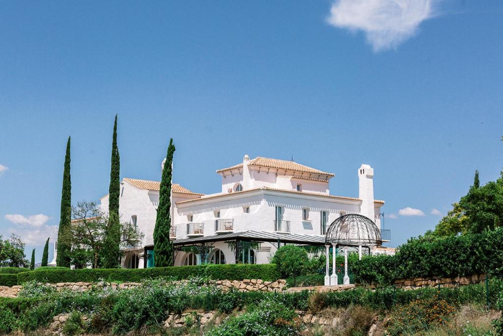 uma grande casa branca numa colina com árvores em B Bou Hotel Cortijo Bravo em Vélez-Málaga