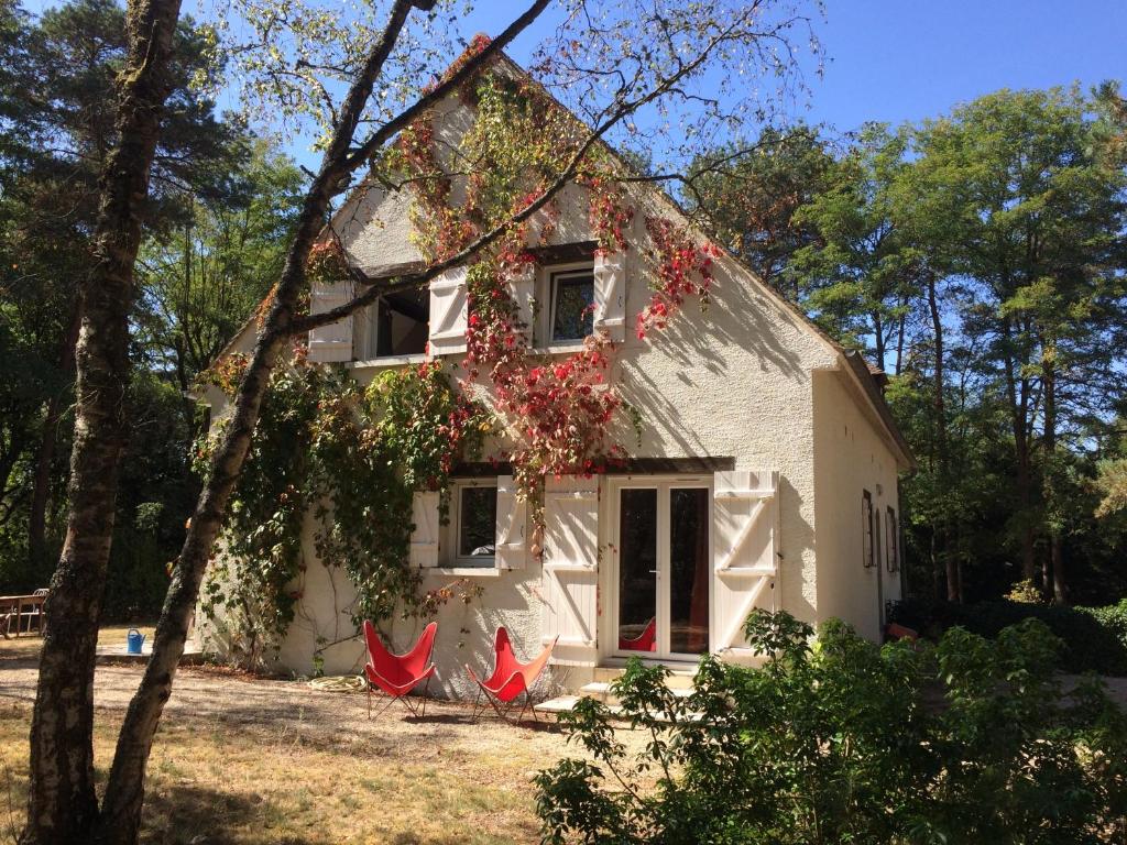 a white house with red chairs in front of it at Chambres au coeur du Massif des Trois Pignons in Noisy-sur-École