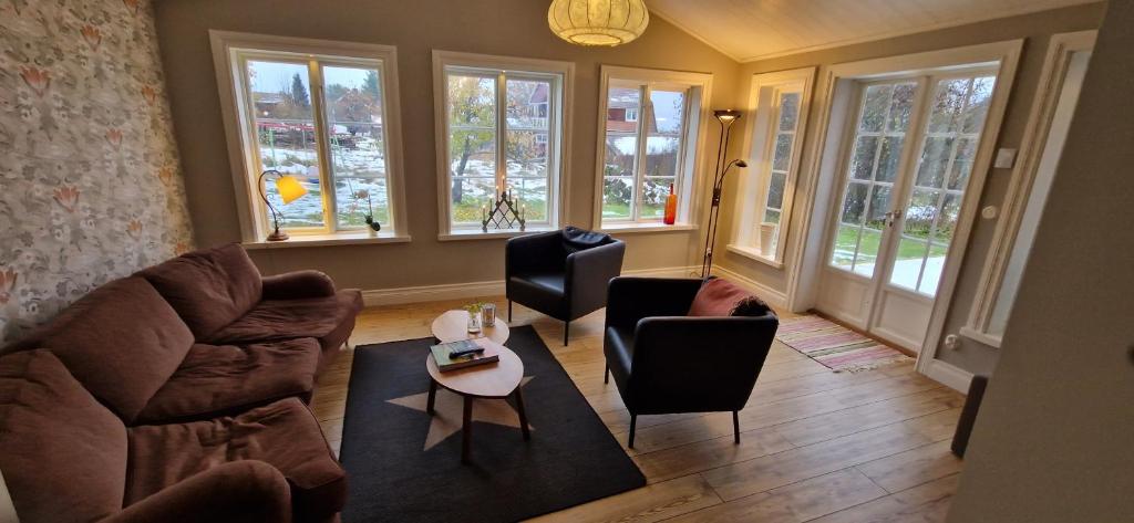 een woonkamer met een bank, stoelen en ramen bij Rymlig dalastuga i Siljansnäs 4-6 bäddar in Siljansnäs