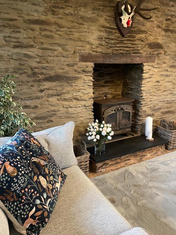 sala de estar con sofá y chimenea de piedra en Winstitchen Cottage, en Simonsbath