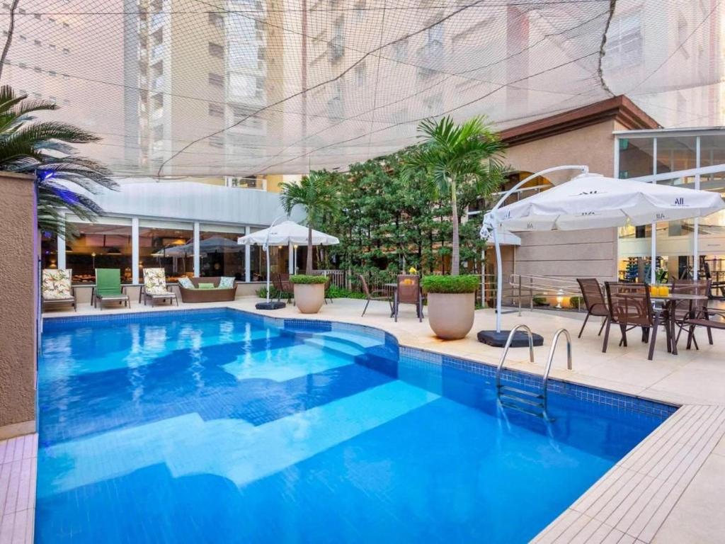 a large blue swimming pool with tables and umbrellas at Flat Funchal JK Vila Olímpia Limpeza Diária in Sao Paulo