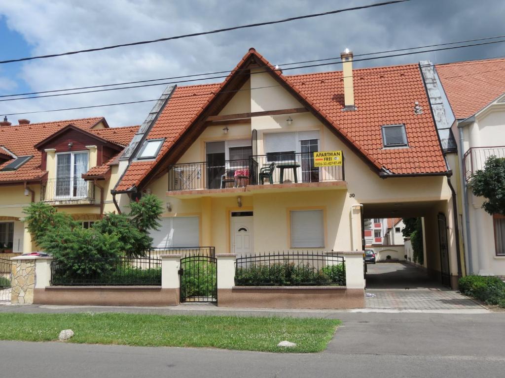 a yellow house with a balcony and a roof at Jázmin Apartman in Harkány