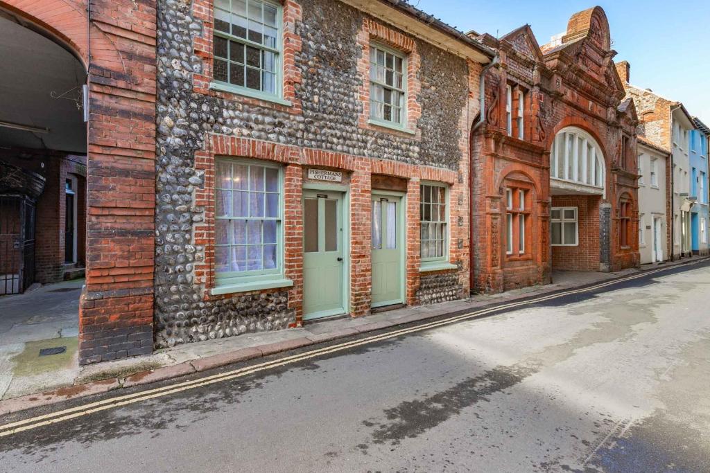 an old brick building with green doors on a street at Fishermans Cottage - Norfolk Holiday Properties in Cromer