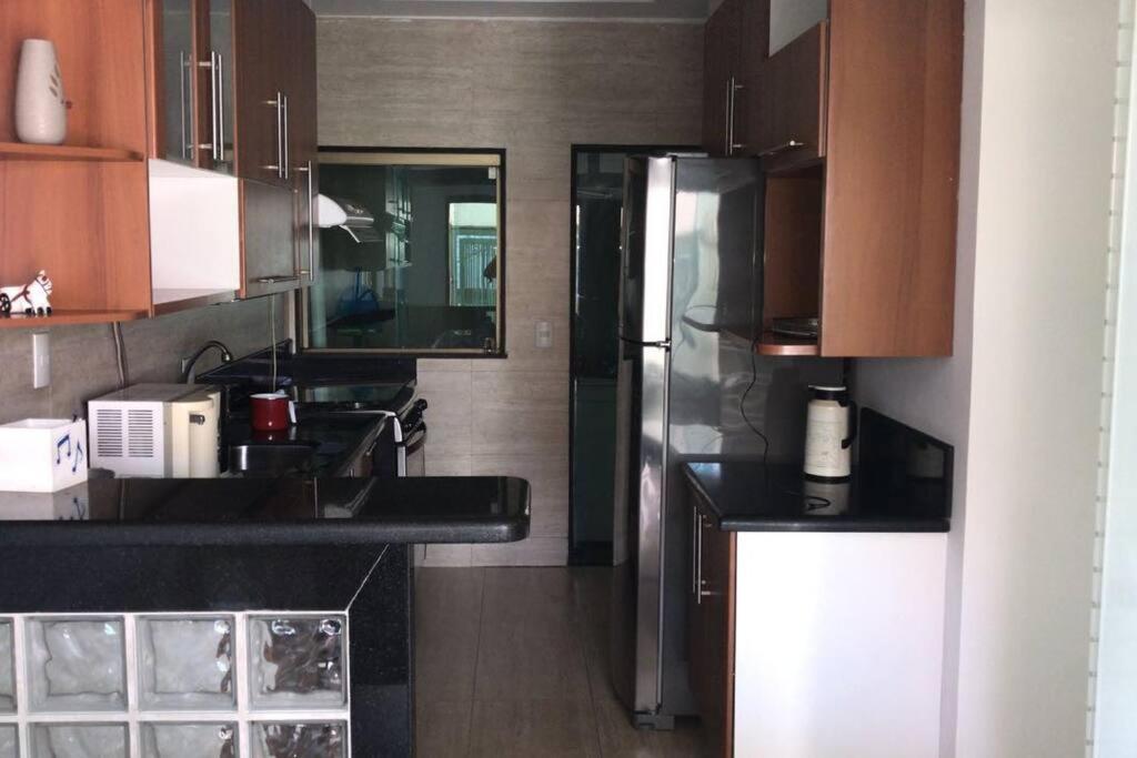 a kitchen with wooden cabinets and a stainless steel refrigerator at Casa confortável p/13/14/18 pessoas c 4/5/6 suítes in Belo Horizonte