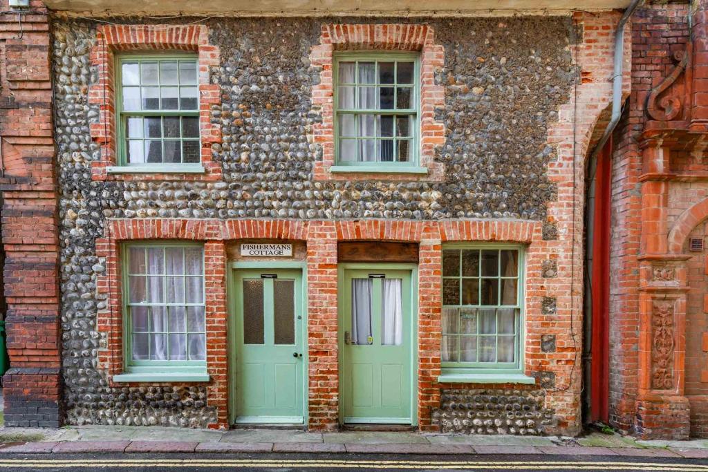 an old brick building with green doors and windows at Shoemakers Cottage - Norfolk Holiday Properties in Cromer