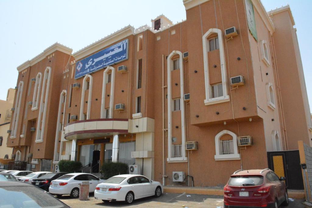duży ceglany budynek z samochodami zaparkowanymi na parkingu w obiekcie العيرى للشقق المخدومه جيزان 3 w mieście Dżizan