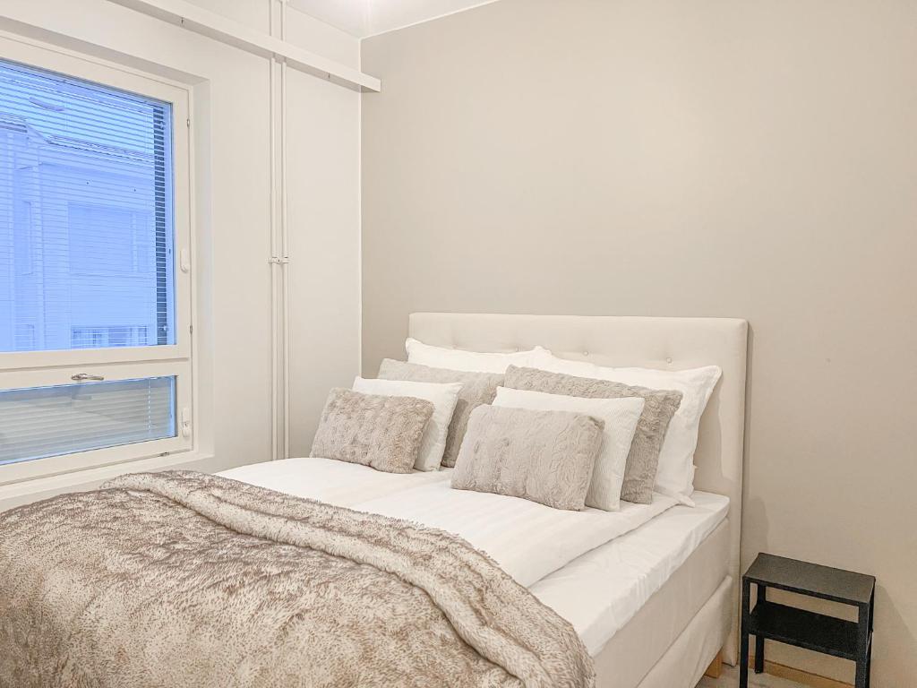 a white bedroom with a bed with pillows and a window at Rollo Apartments in Rovaniemi