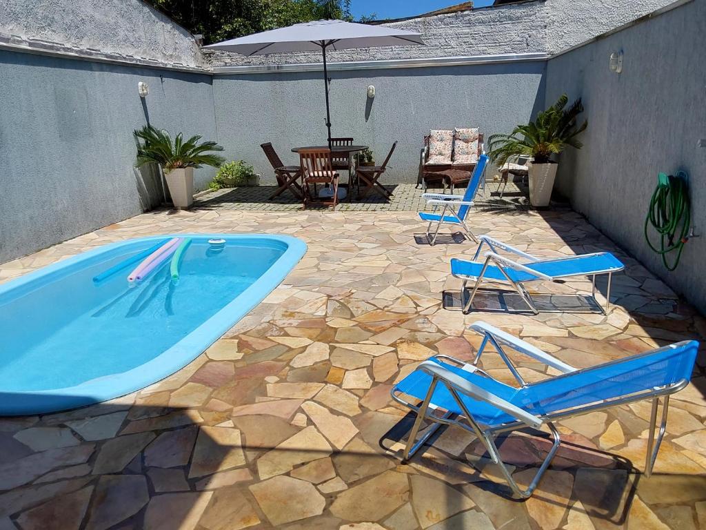 グァラトゥバにあるCasa com piscina duas quadras da praiaのスイミングプール、椅子2脚、パラソル1本が備わります。