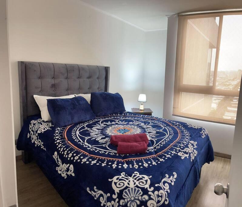 a bedroom with a blue and white bed with a window at Apartamento en Metro Ñuble in Santiago