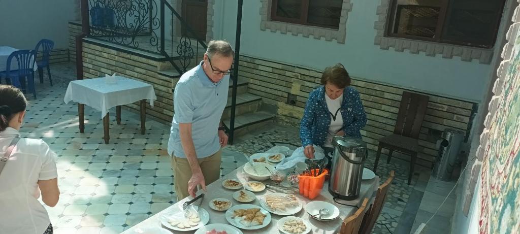un hombre y una mujer parados alrededor de una mesa con comida en Uzbegim Family Guest House, en Bukhara