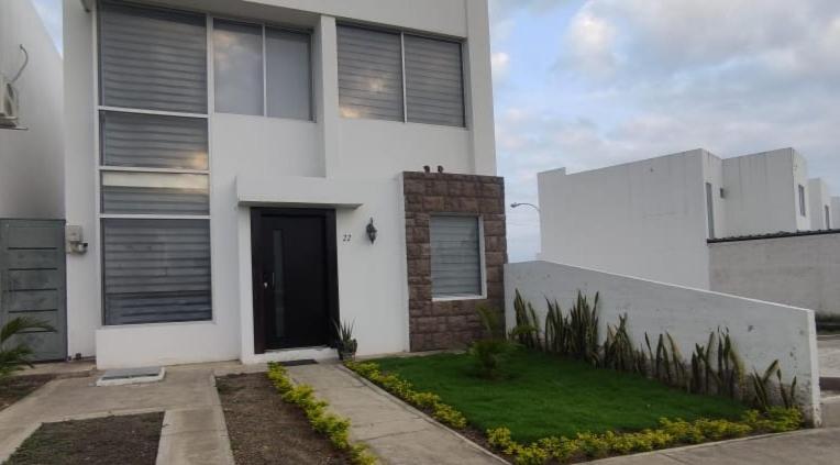 een wit huis met een zwarte deur en een tuin bij Moderna casa con piscina y cerca de la playa in Manta