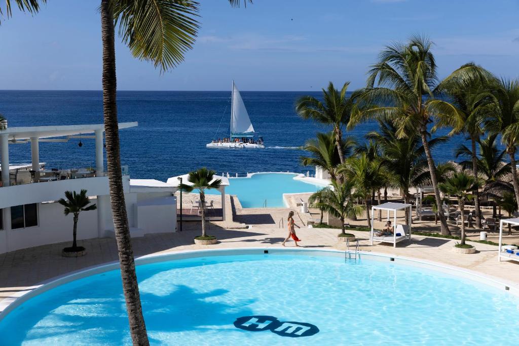 a swimming pool with a sailboat in the ocean at HM Alma de Bayahibe - Adults Only in Bayahibe