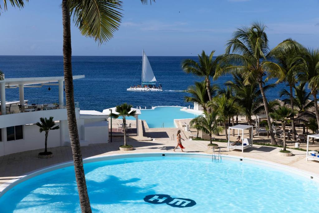 ein Pool mit einem Segelboot im Ozean in der Unterkunft HM Alma de Bayahibe - Adults Only in Bayahibe